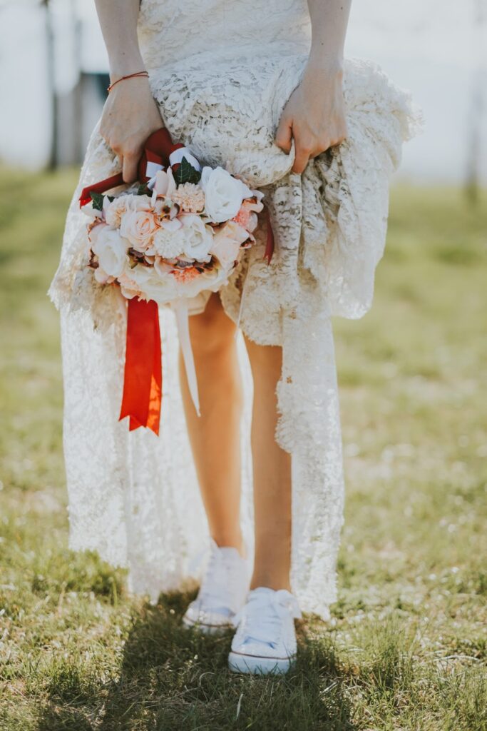 Mujer con vestido de novia estilo boho con ramo de flores en la mano con zapatillas blancas